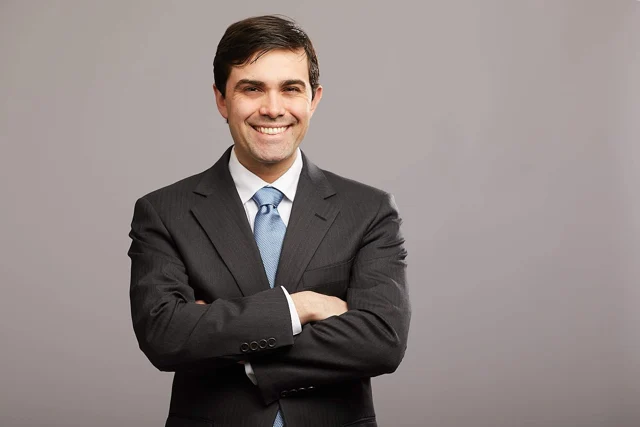 Ryan in a dark suit and blue tie, smiling with his arms folded.