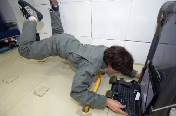 Ryan in a flight suit floating above a laptop inside the padded cabin of the reduced-gravity aircraft.
