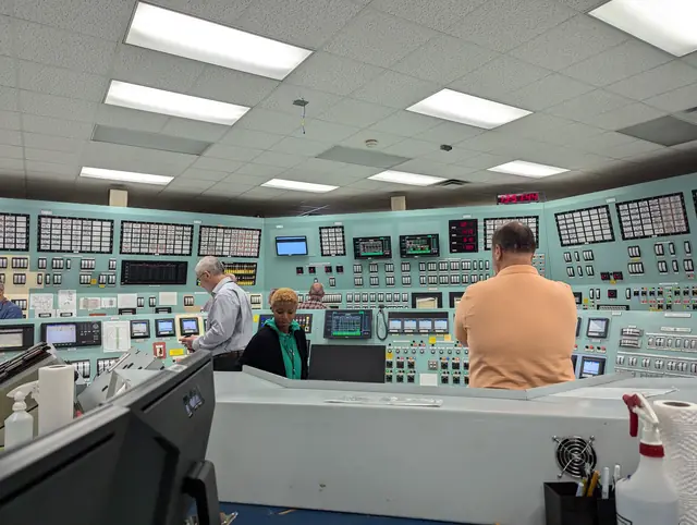Visitors in a control room lined with instrument panels, switches, and monitors.