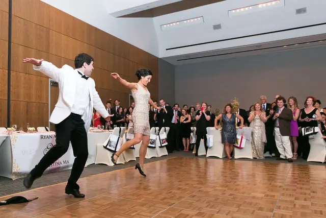 A couple dancing at a wedding reception, with guests watching from the edge of the dance floor.