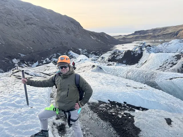 A hiker with a helmet, sunglasses, and an ice axe stands on a glacier.